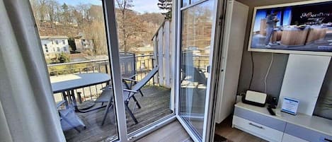 A modern interior with a sliding glass door leading to an outdoor deck, a flat-screen TV on a white cabinet, and a small table with chairs.