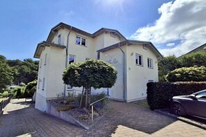 A two-story building with a flat roof, a small tree in front, and a car parked to the side. - Holiday apartment with 1 bedroom (Heringsdorf (Seebad))