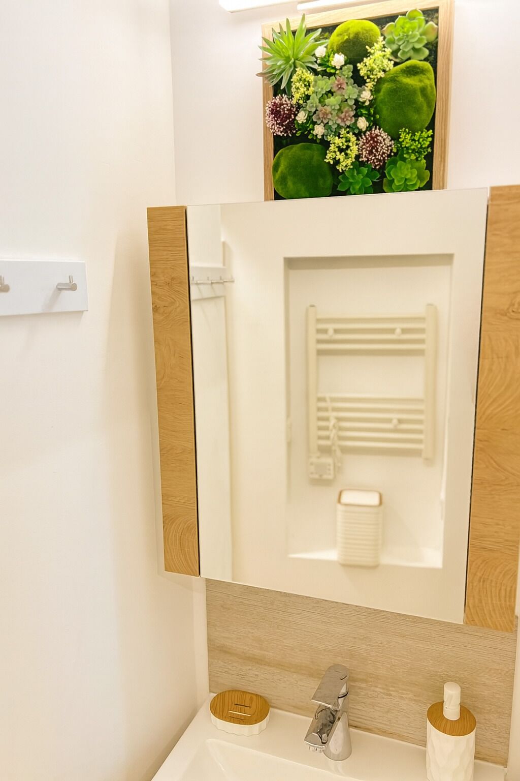Une salle de bain avec un miroir, un porte-serviettes, un lavabo et un mur décoratif végétal.