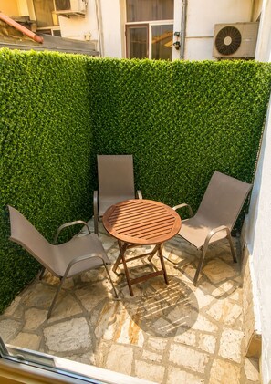 Eine Terrasse mit einem runden Tisch und zwei Stühlen, umgeben von einer grünen Hecke.
