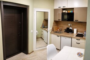 Une cuisine compacte avec une porte sombre, des placards blancs, un plan de travail en bois et une petite table à manger sur laquelle se trouve un bol de collations.