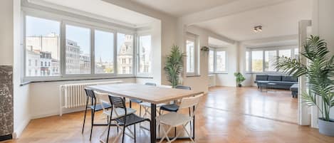 A spacious living area with a large table and chairs, a sofa, and several potted plants.