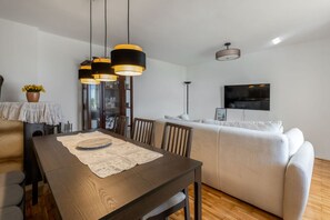 Ein modernes Wohnzimmer mit einer Couch, einem Esstisch mit Platzsetzer und Pendelleuchten.