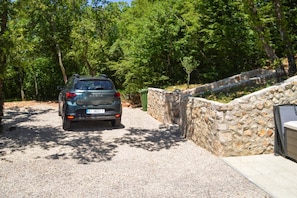 Ein geparktes Auto auf einer Auffahrt mit einer Steinmauer und Bäumen im Hintergrund.