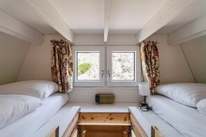 Een kamer met twee bedden, een raam met gordijnen, een bedlampje en een kleine verwarming.