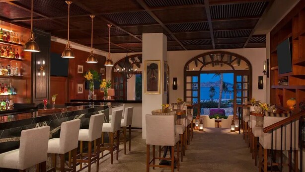 A bar area with a counter, bar stools, and a view of the sea through an arched doorway. - Zoëtry Casa Del Mar Los Cabos One Bedroom Suite Ocean View (San José del Cabo)