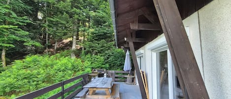 Une terrasse en bois aménagée à l’extérieur, avec des tables de pique-nique, entourée d’une forêt dense.