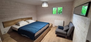 A bedroom with a wooden bed, a grey sofa, a window with a view of greenery, and a ceiling light.