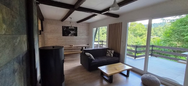 A modern living room with a sofa, a coffee table, and a large window offering a view of greenery.