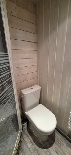 A small bathroom with a white toilet, wooden panel walls, and a tiled floor.