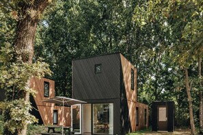 Een modern houten chalet met twee verdiepingen en een glazen deur, omgeven door een dicht bos.