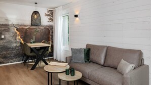 A cozy living room with a sofa, a dining table, and chairs. There is a wall-mounted light fixture and a window with curtains. - Villa in Schaijk near Forest & Water (Schaijk)