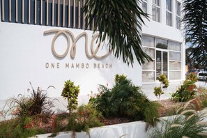 Ein Hotelschild mit dem Namen 'ONE MAMBO BEACH' und einer modernen Gebäudefassade.