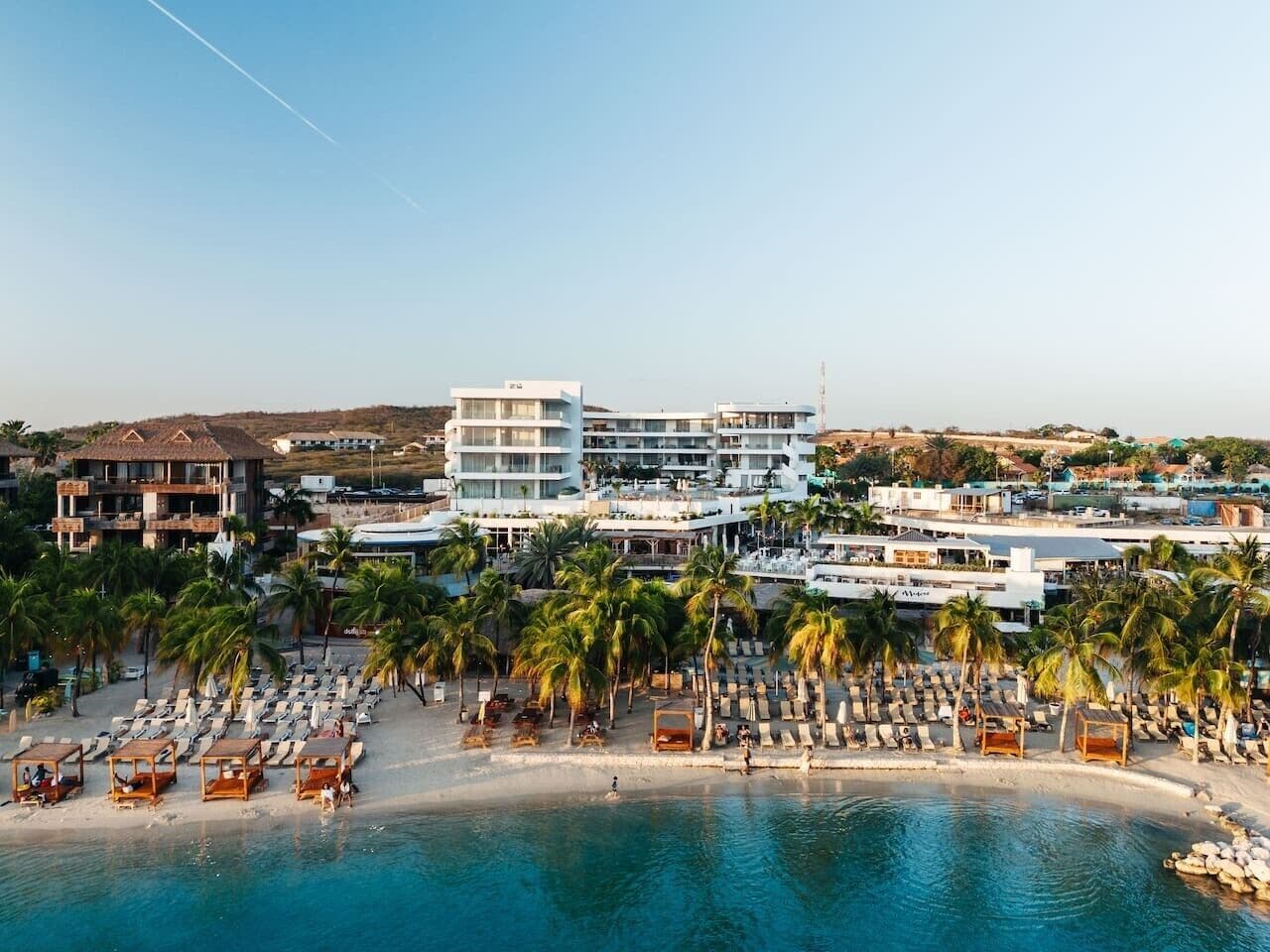 A coastal hotel with multiple buildings, a beach with sun loungers, and a pool.