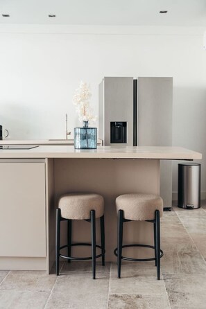 Eine moderne Küche mit einer zentralen Kochinsel, zwei Barhocker, einem Mülleimer und einem Kühlschrank.