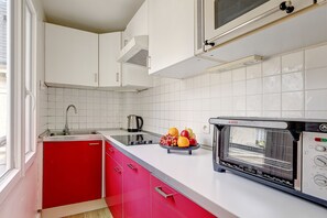 A kitchen with white tiles, a red cabinet, a sink, a kettle, and a toaster oven. - Charming Stay Near Louvre & Palais Royal (Paris)