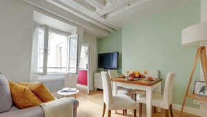 Un soggiorno con un divano, un tavolo da pranzo con sedie, una televisione e una finestra con tende.