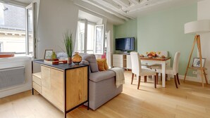 Un soggiorno moderno con un divano grigio, un mobiletto in legno, un'area pranzo con tavolo e sedie, una televisione e una finestra con vista sull'esterno.