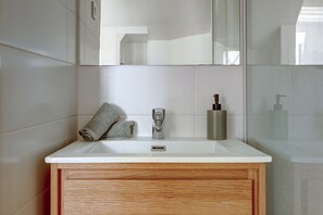 A bathroom with a white sink, wooden vanity, and a mirror above it. - Charming Stay Near Louvre & Palais Royal (Paris)