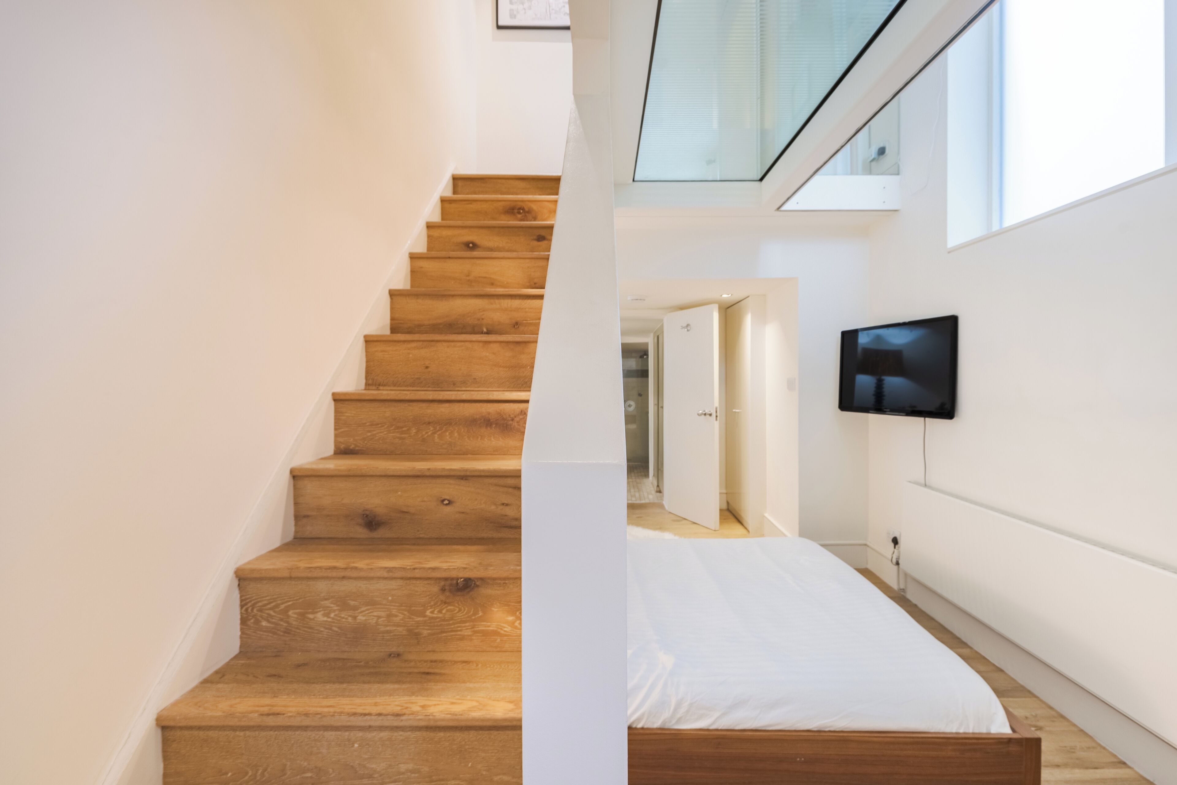 A staircase with wooden steps leading to a room with a bed and a television mounted on the wall.
