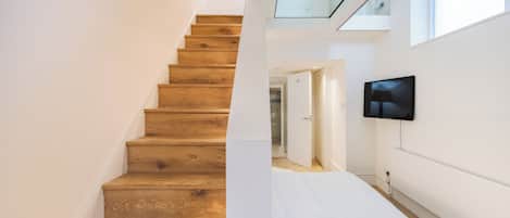 A staircase with wooden steps leading to a room with a bed and a television mounted on the wall.