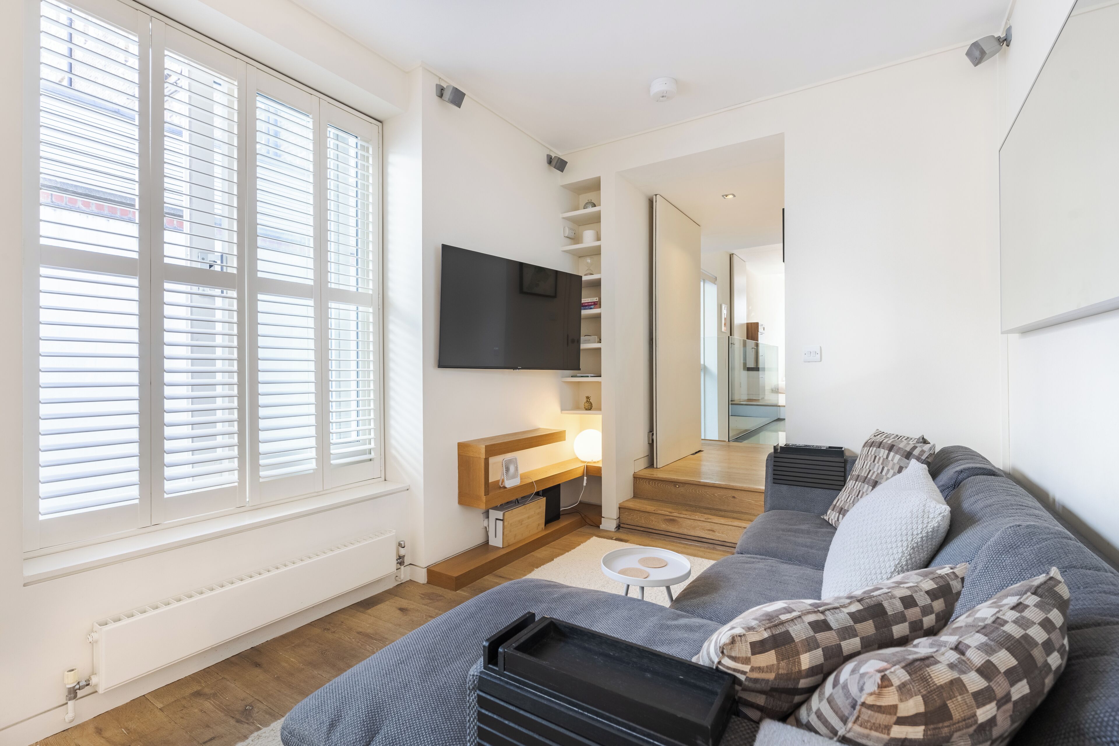 Un salon moderne avec un canapé, un téléviseur à écran plat fixé au mur et un escalier menant à l’étage supérieur.
