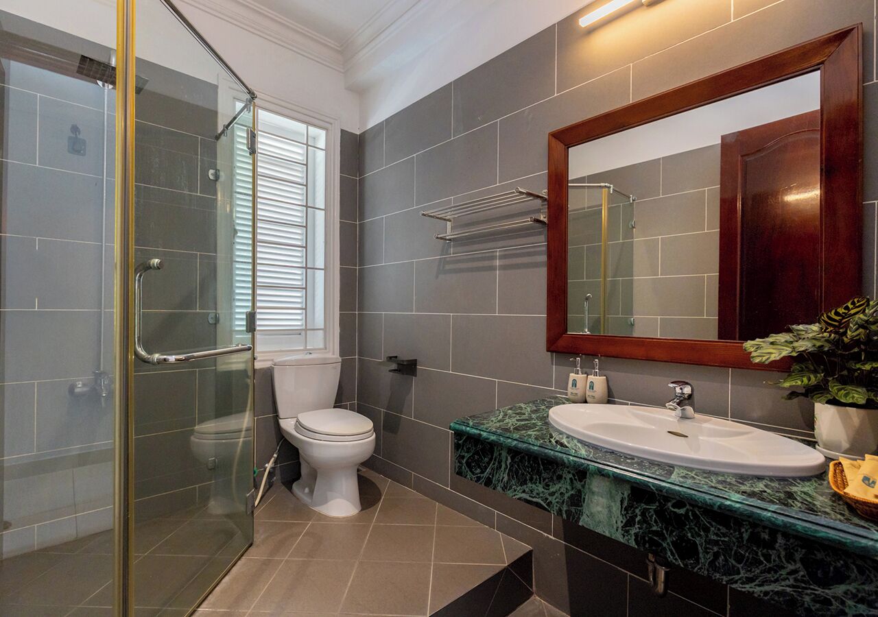 A modern bathroom with a glass shower enclosure, a white toilet, a marble countertop sink, and a large mirror.