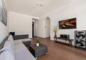 A modern lounge area with a sofa, a small table with a plant, a bench, and a wall-mounted TV displaying a jazz album.