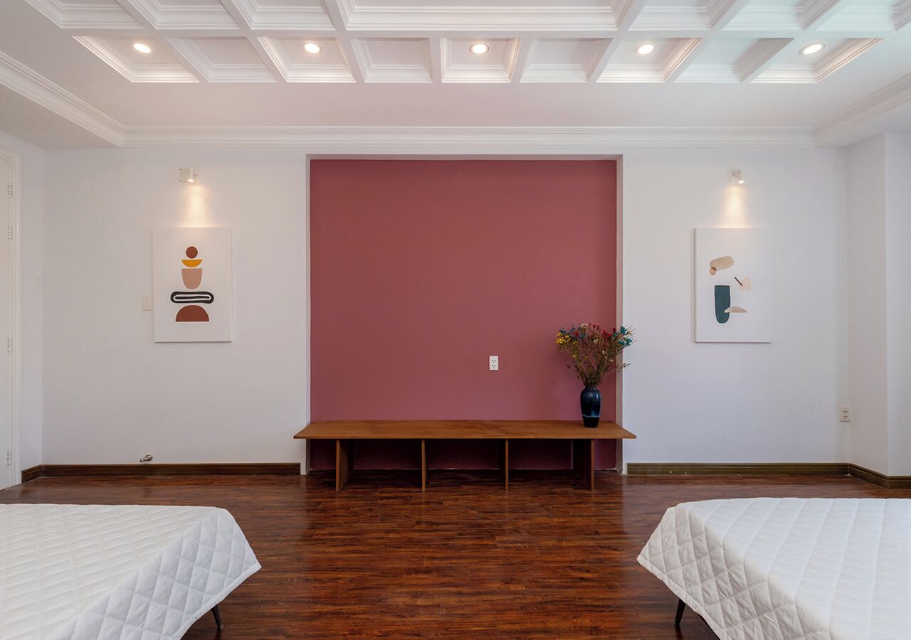 Une pièce avec deux lits, un banc et un grand mur rose.