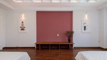 A room with two beds, a bench, and a large pink wall.