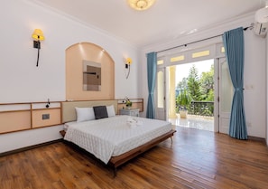 A spacious bedroom with a large bed, wooden flooring, a built-in bench, and a view of the outdoors.