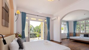 Ett hotellrum med en stor säng, en mindre säng, en balkong med gardiner och utsikt över grönområden utanför.