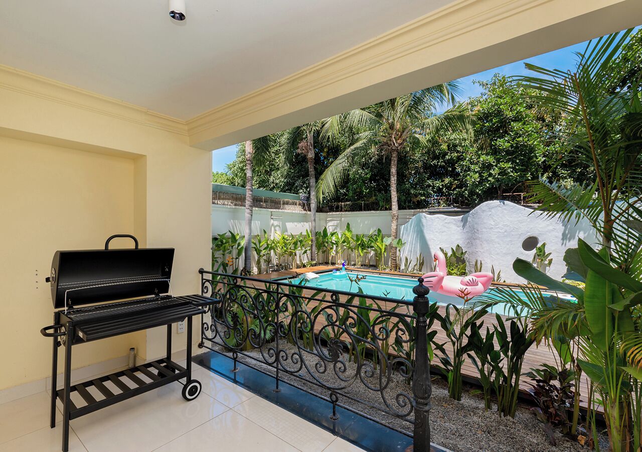 Un balcon avec un barbecue, une piscine et des plantes tropicales.