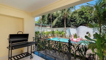 Un balcon avec un barbecue, une piscine et des plantes tropicales.