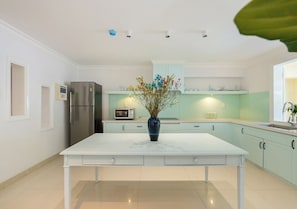 Cocina moderna con una mesa blanca, un refrigerador de acero inoxidable, un microondas y un florero con flores.