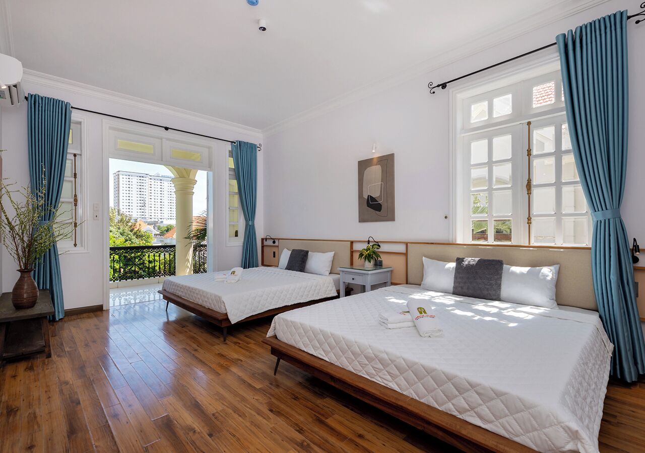 A hotel room with two beds, a wooden floor, a balcony, and a view of the city.