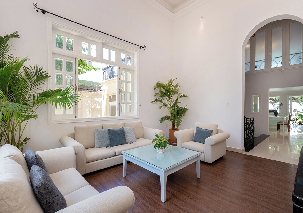 A spacious living room with a large window, a sofa set, a coffee table, and a potted plant.
