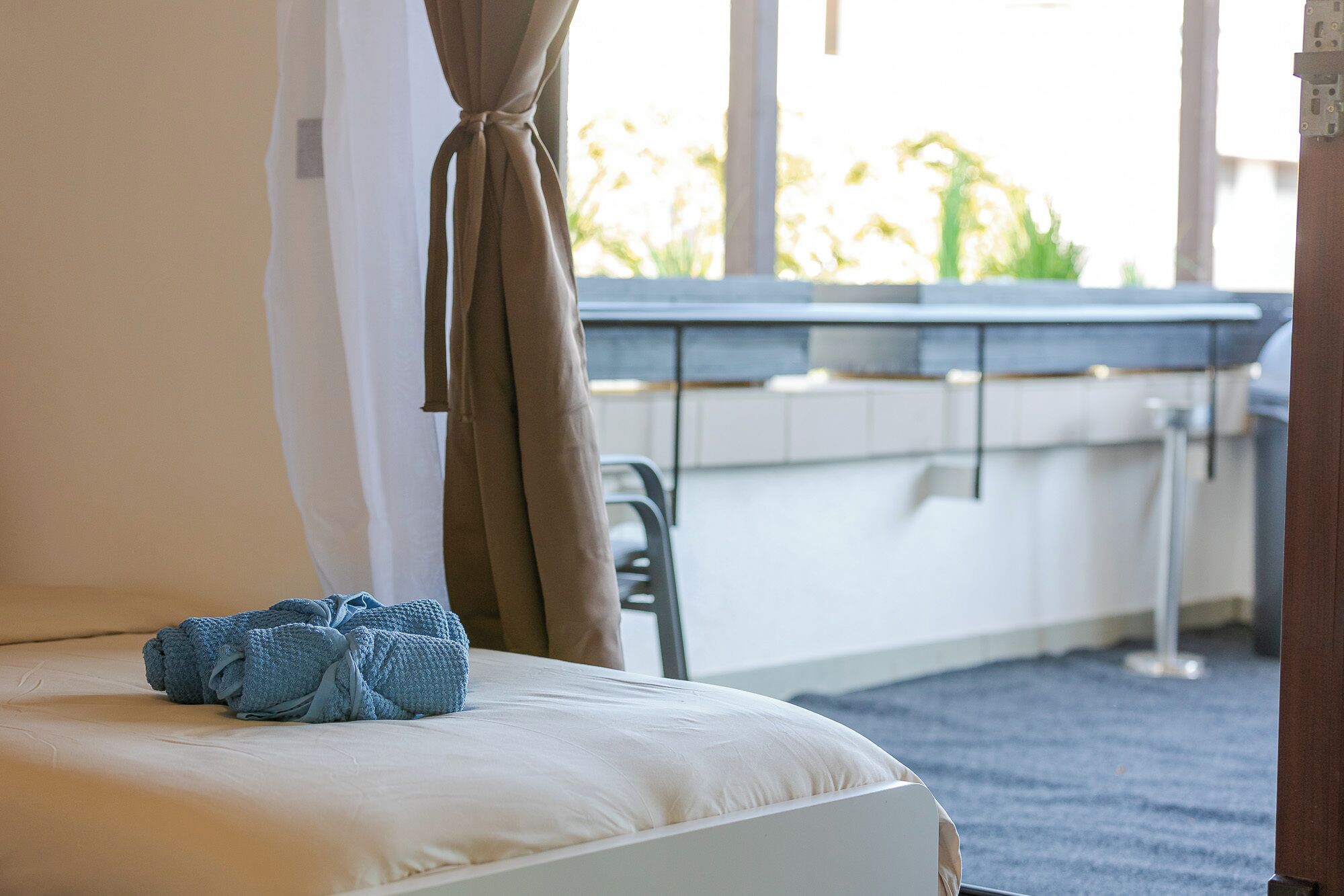 Ein Hotelzimmer mit einem Bett, einem Vorhangfenster, Blick auf Grün und einem kleinen Tisch mit Stuhl.