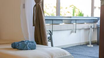 Ein Hotelzimmer mit einem Bett, einem Vorhangfenster, Blick auf Grün und einem kleinen Tisch mit Stuhl.