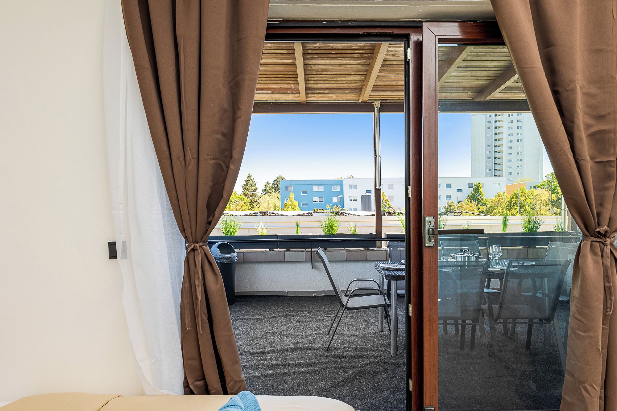 A balcony with a table and chairs, a view of buildings, and curtains.