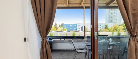 A balcony with a table and chairs, a view of buildings, and curtains.