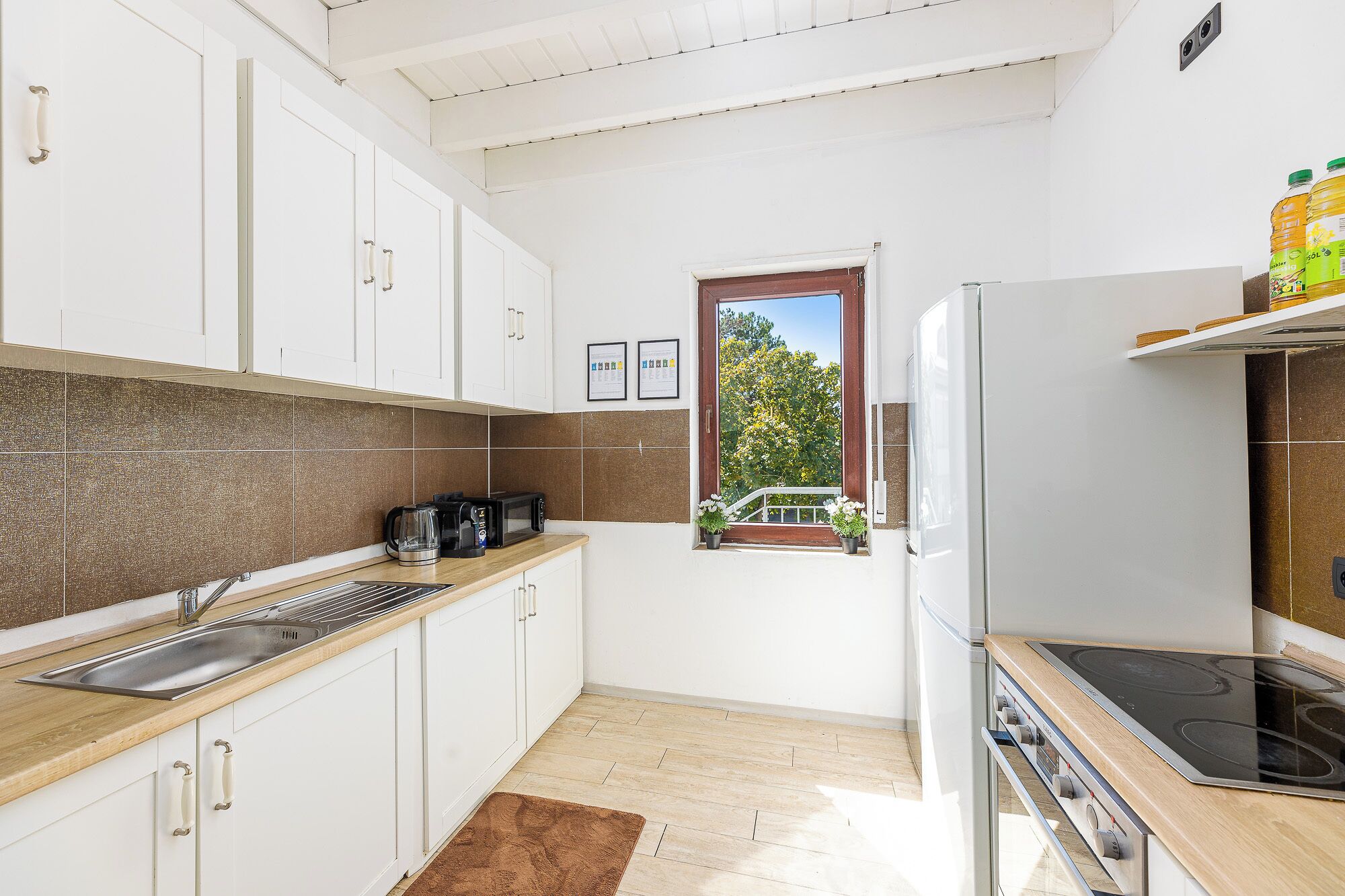 Eine Küche mit weißen Schränken, einer Holz Arbeitsplatte, einem eingebauten Ofen und einem Fenster mit Blick auf Bäume.