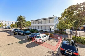 Um estacionamento com vários carros, um edifício com grandes janelas e um céu claro.