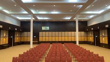 A conference room with rows of chairs, a stage, and a large screen.