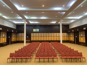 A conference room with rows of chairs, a stage, and a large screen.