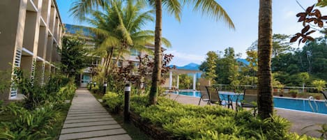 A pathway leading to a pool area with palm trees and a building with a balcony.