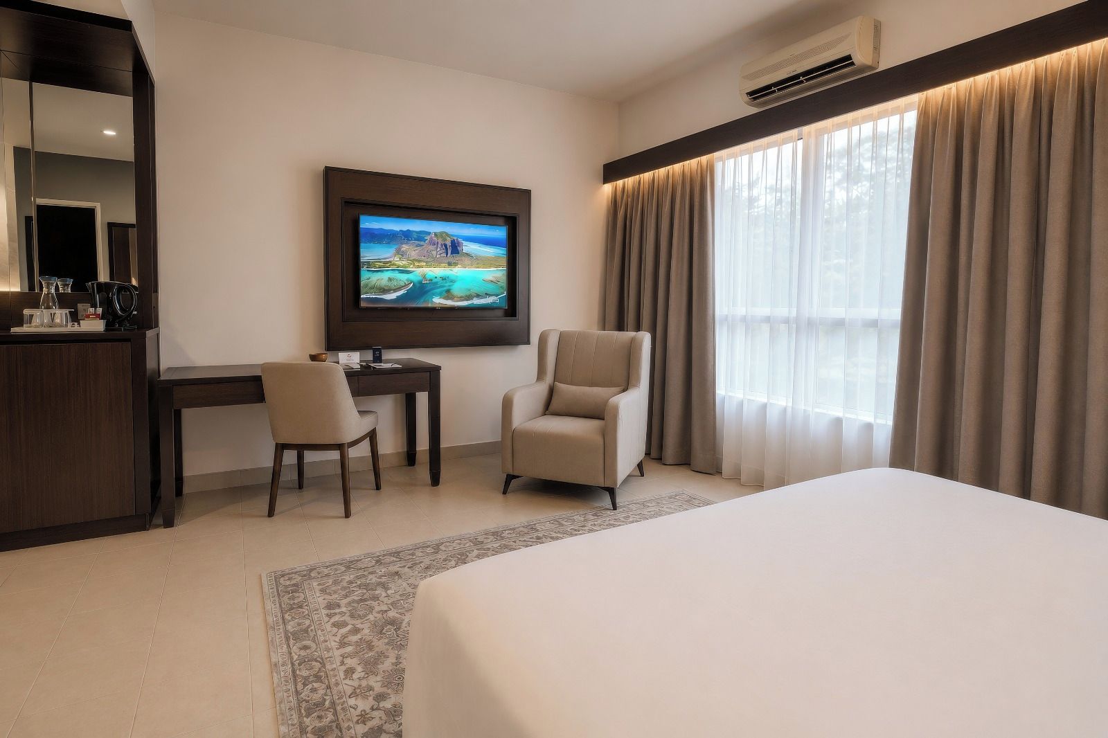 Habitación de hotel con cama, escritorio, silla, televisor y ventana con cortinas.