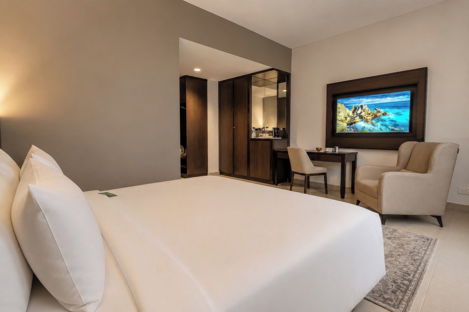 Una habitación de hotel con una cama grande, un escritorio, una silla y un televisor montado en la pared.