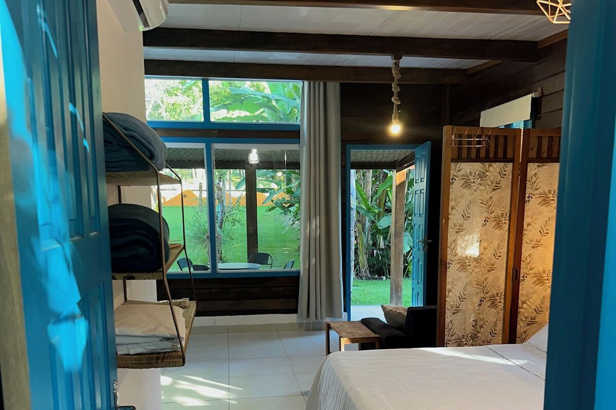 Ein Schlafzimmer mit Bett, einer Bank, einem Tisch und Blick ins Freie.