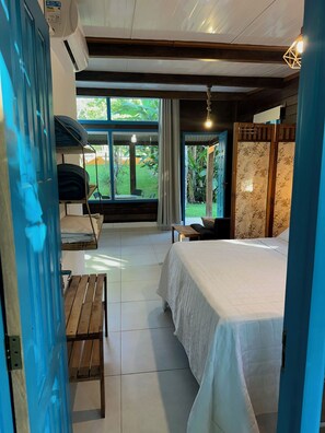 Ein Schlafzimmer mit Bett, einer Bank, einem Tisch und Blick ins Freie.